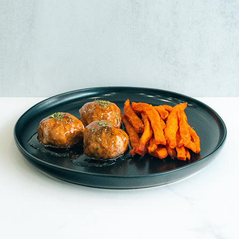 Bourbon Turkey Meatballs served on a sleek black plate with herbs and sweet potato fries, set against a light background—the perfect high-protein meal prep option.