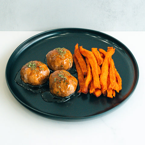 Bourbon Turkey Meatballs served with sweet potato fries on a black plate, garnished with fresh herbs—a tasty, macro-friendly option perfect for a nutritious meal.