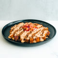 A black plate with crispy fried potato cubes topped with creamy sauce, ground meat, and a small mound of fresh pico de gallo in the center.