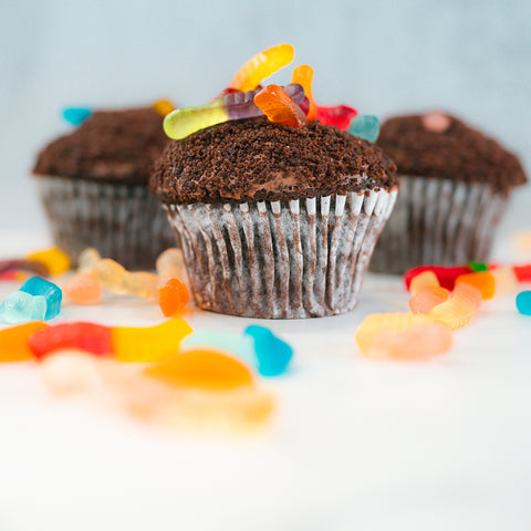 Buffin Muffin Dirt Cake, a nostalgic chocolate cupcake dessert, topped with gummy worms and surrounded by colorful gummy candies on a white surface.