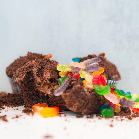 The Buffin Muffin Dirt Cake features crumbled chocolate muffins topped with colorful gummy worms, both on and around the dessert, set against a light background for a playful throwback treat.