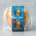 A clear plastic container holds a yellow muffin. The blue label reads Buffalicious Baddie Blueberry Blondie and features images of blueberries and a cartoon woman with red hair. Nutritional info is listed at the bottom.