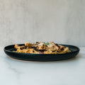 A black plate with Gluten Free Carbonara Chicken Subscription—high-protein pasta topped with grilled chicken, grated cheese, and herbs—set on marble against a neutral backdrop, for perfect Italian comfort food.