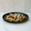 A black plate with Gluten Free Carbonara Chicken Subscription—high-protein pasta, grilled chicken strips, veggies, and grated cheese—rests on a white marble surface against a light backdrop.