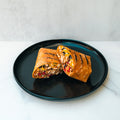 The Hey Arnold Burrito, packed with chicken, corn, black beans, and veggies, is sliced in half and served on a black plate—an ideal high-protein meal for post-workout satisfaction.