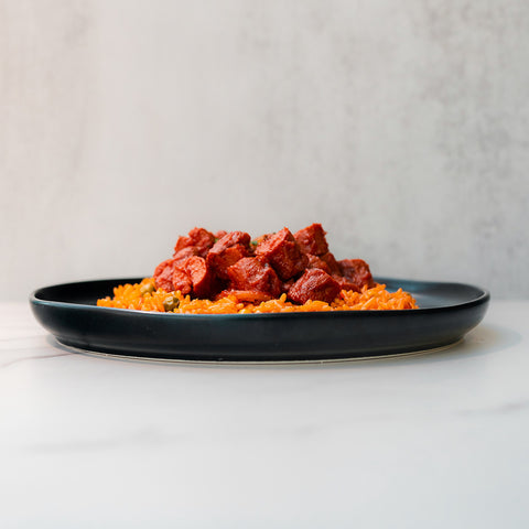 A black plate of Smoky Beef Sausage and Rice—orange jasmine rice topped with smoky beef sausage pieces, set on a light surface with a plain background—perfect comfort food.