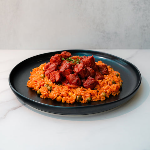 Smoky Beef Sausage and Rice features jasmine rice with peas and corn, topped with smoky beef sausage chunks and stewed meat on a black plate—a comfort meal perfect for any time.