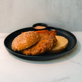 The Chicken Veggies Burger, featuring a high-protein chicken patty on a sesame seed bun, is served open-faced on a black plate with sweet potato fries and dipping sauce.