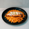 Farfalle Chicken Alfredo: High-protein pasta in creamy orange sauce with grilled chicken, melted cheese, and green peppers—a delicious ready-to-heat meal, plated on black against a white surface and light gray background.