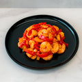 A black plate of Hawaiian Pineapple Shrimp 1lb is served with red and yellow bell pepper slices, displayed on white marble for a colorful, high-protein entrée.