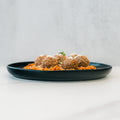 A black plate features Garden Orzo Meatballs topped with grated cheese, set on a white surface and light grey background—an ideal high-protein meal prep option.
