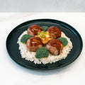 A black plate features white rice topped with Pineapple Teriyaki Meatballs, pineapple pieces, chopped green onions, and broccoli florets—a perfect high-protein meal prep using Pineapple Teriyaki Meatballs.