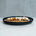 Anatolian Kebab Bulgur Rice features sliced grilled chicken breast and tender thighs with creamy white sauce, served over bulgur wheat for a Mediterranean-style meal on a dark plate against a light gray background.