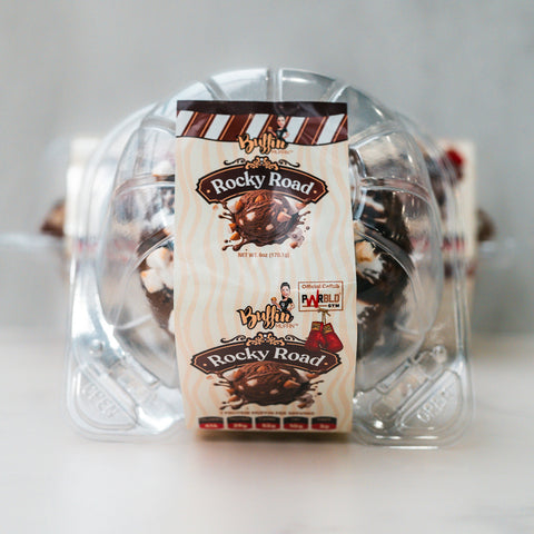 Clear plastic container holds VIP Buffin - Rocky Road, featuring an image of chocolate-covered treats. Label highlights macro-friendly snack flavor, net weight 8oz, allergen info, and quality certification.