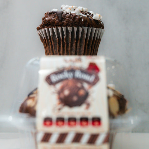 A close-up of the VIP Buffin - Rocky Road shows white marshmallow bits atop a chocolate muffin in a plastic container. Ideal as a macro-friendly snack, its label is blurred in the foreground against a light background.