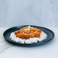 BBQ Meltdown features a black plate with white rice, fried tofu cubes, shredded cheese, ground meat, pickles, and diced onions—ideal for high-protein meal prep—presented on a marble surface against a light gray background.