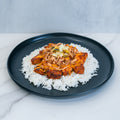 The BBQ Meltdown is served on a black plate: white rice topped with seasoned chicken, shredded cheese, ground meat, and diced veggies—perfect for high-protein meal prep on a marble surface.