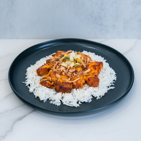 The BBQ Meltdown is served on a black plate: white rice topped with seasoned chicken, shredded cheese, ground meat, and diced veggies—perfect for high-protein meal prep on a marble surface.
