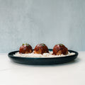 A dark plate features a high protein rice bowl topped with Caribbean Jerk Meatballs covered in sauce and herbs against a light background—Caribbean Jerk Meatballs are perfect for easy, flavorful meal prep.