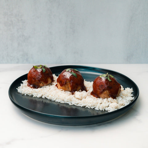 Caribbean Jerk Meatballs glazed in barbecue sauce and herbs are served over high-protein rice, creating a flavorful and meal-prep friendly bowl, beautifully presented on a dark plate against a light background.