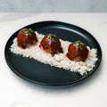 Three Caribbean Jerk Meatballs garnished with herbs rest on a bed of white rice, served on a black plate against a marble background—a high-protein, easy meal prep rice bowl.