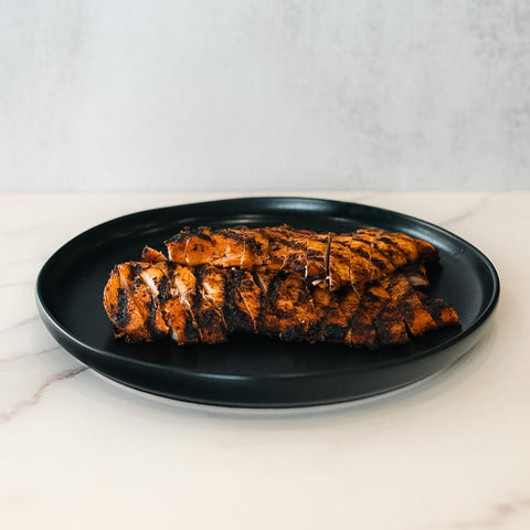 Chipotle Chicken 1lb Competition Approved features sliced, pre-cooked grilled chicken breast with char marks, arranged on a black plate—ideal for meal prep or healthy dinners.