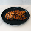 Sliced, grilled Chipotle Chicken 1lb Competition Approved with visible char marks, neatly arranged on a black plate atop white marble—ideal for a healthy dinner.
