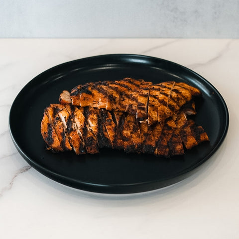 Sliced, grilled Chipotle Chicken 1lb Competition Approved with visible char marks, neatly arranged on a black plate atop white marble—ideal for a healthy dinner.