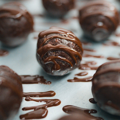 Close-up of 3 Banana Chocolate Protein Poppers on a light surface, each coated in glossy chocolate drizzle. The focus is on the center popper, showing its smooth finish—a delicious and healthy snack option.