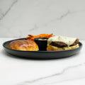 Burger with cheese, bun, and side of fries on a black plate against a marble background