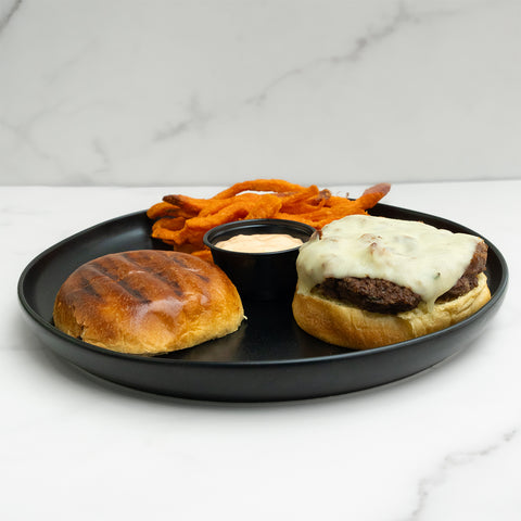 Burger with cheese, sweet potato fries, and a side of sauce on a black plate.