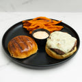 Burger with cheese, sweet potato fries, and a side of sauce on a black plate.