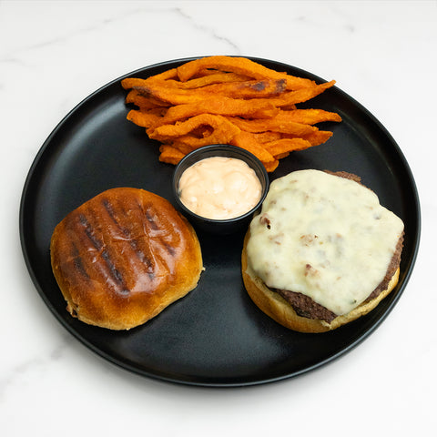 Burger with cheese, sweet potato fries, and a side of sauce on a black plate.