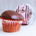 Buffin Muffin Red Velvet with a chocolate-covered top sits in front, its clear packaging and red-and-white "Red Velvet" label visible behind—ideal for anyone craving a delicious protein dessert.
