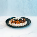 Olympian Chicken Gyro Bowl - Exclusive featuring sliced seasoned chicken over rice, topped with crumbled cheese and sliced black olives on a black plate.