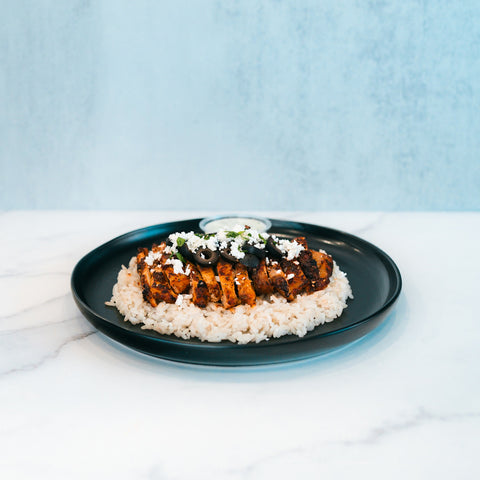 Olympian Chicken Gyro Bowl - Exclusive featuring sliced seasoned chicken over rice, topped with crumbled cheese and sliced black olives on a black plate.