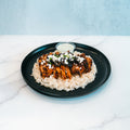Olympian Chicken Gyro Bowl featuring sliced seasoned Hummus Fit chicken over rice, topped with crumbled cheese and sliced black olives, served with a side of sauce on a black plate.