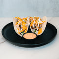 Baja Chicken Tacos: Grilled chicken, shredded cheese, and veggies in low-carb tortillas served on a black plate with creamy dipping sauce, set against a light marble background.