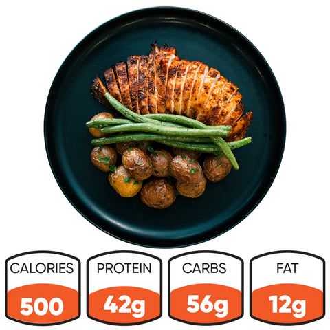 Baked Herb Chicken and Potatoes—sliced chicken breast, green beans, and roasted potatoes on a black plate. Perfect for meal prep. Nutrition: 500 calories, 42g protein, 56g carbs, 12g fat.