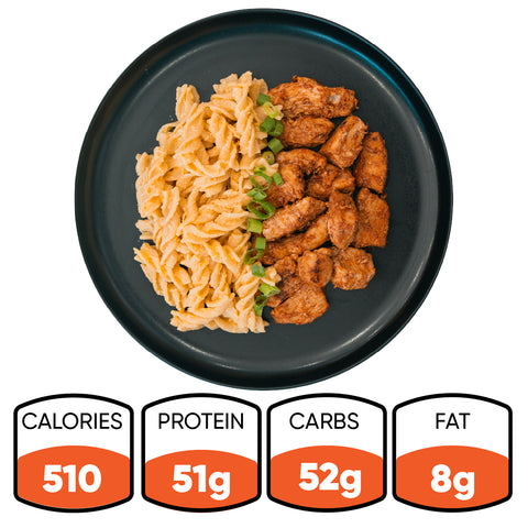 A black plate with BBQ Chicken Mac Bowl pasta, garnished with green onions. This Hummus Fit healthy meal prep has 510 calories, 51g protein, 52g carbs, and 8g fat.