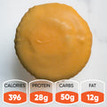The Buffin Muffin VIP - Buffalicious Baddie, a round yellow-frosted high-protein muffin, sits on a white surface. Nutrition: 396 calories, 28g protein, 50g carbs, and 12g fat—an ideal gym-friendly snack.
