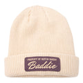 A cream-colored, cuffed rib-knit beanie with a folded brim, featuring a purple patch that reads PROPERTY OF BUFFIN BAKERY Baddie in white—perfect for gym-to-street athleisure looks.