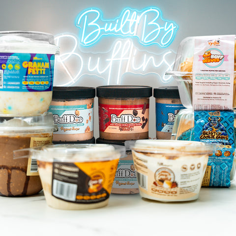 An assortment of Buff Doe dessert containers and tubs are arranged on a counter, with a glowing Built By Buffins neon sign in the background.