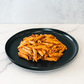 The Clean Bulk Pasta Bowl features healthy pasta with red tomato sauce and ground meat, served on a black plate atop white marble and a light gray background—ideal for high-protein meal prep.