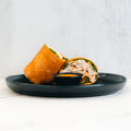 The Club Wrap, packed with chicken, greens, and veggies, is served halved on a black plate with dipping sauce—an ideal high-protein meal prep choice against a clean, light background.