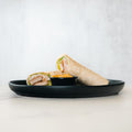 The Crispy Vegan Wrap features two protein- and fiber-packed halves on a black plate with a side of dipping sauce. Set against a plain, light background—it's the perfect healthy lunch option.