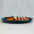 Fit A La Vodka With Chicken features penne pasta in vodka sauce, topped with sliced grilled chicken, white onions, and fresh herbs—a healthy meal served on a dark plate against a light background.