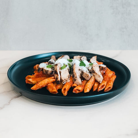 Fit A La Vodka With Chicken features penne pasta in a vibrant red sauce with grilled chicken breast, drizzled with white sauce and garnished with fresh herbs for a healthy, delicious meal.