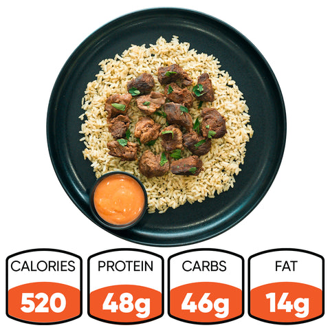 The “GLORIOUS GAINS” Steak Bites Cilantro Lime Rice features tender beef over cilantro lime rice with green garnish and an orange dipping sauce. Each bowl has 520 calories, 48g protein, 46g carbs, and 14g fat—ideal for high-protein meal prep.