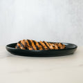 Competition Approved Grilled Chicken 1lb features sliced, halal chicken breast with visible char marks, arranged on a round black plate—ideal for meal prep and presented on a light surface with a neutral background.